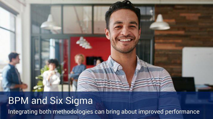 A man smiling into the camera with other employees in the background of the office and a banner across the bottom of the picture that reads "BPM and Six Sigma".