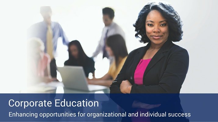 A sign that says "Corporate Education" with a business woman behind it smiling and five more co-workers in the background on a computer and talking to each other.