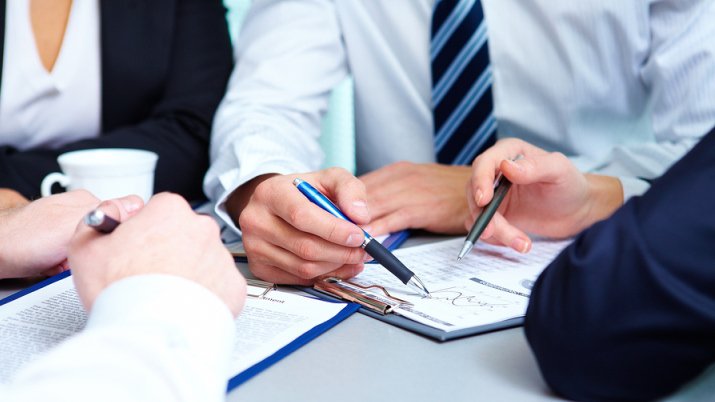 Hands of a business professional writing with a pen on a contract on a clipboard.