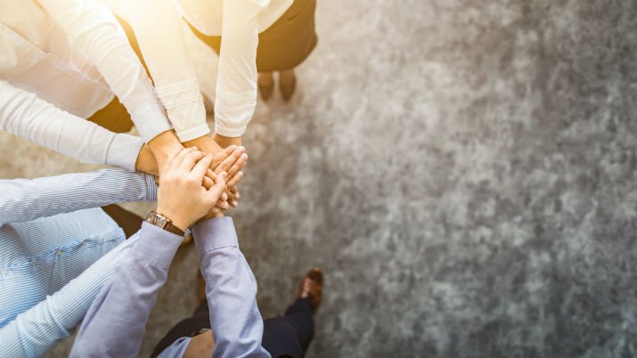 Overhead view of a group of people with their hands in the circle on top of each other as a representation of teamwork and globalization of HR leadership.