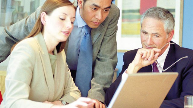 Three business people working together at a computer.