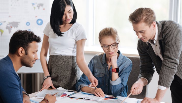 A group of HR employees standing around a table focusing on one book, working together on company initiatives.