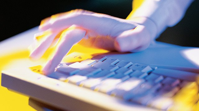 A hand quickly typing on a computer keyboard with yellow hued lighting.