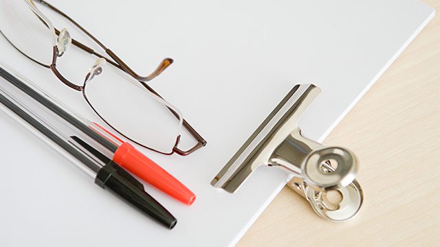 A white clipboard with glasses and a black and red pen sitting on top of it.