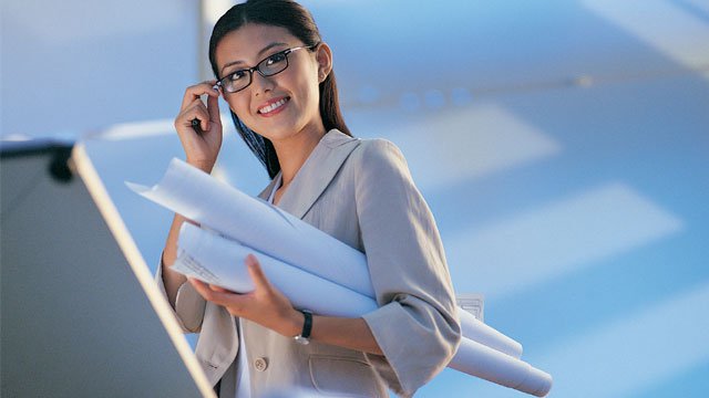 A woman smiling and walking while holding large rolled up papers.