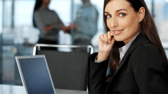 A woman dressed in a suit working on her computer.