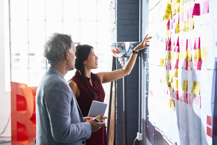 Man and woman looking at colorful adhensive notes on whiteboard in an office