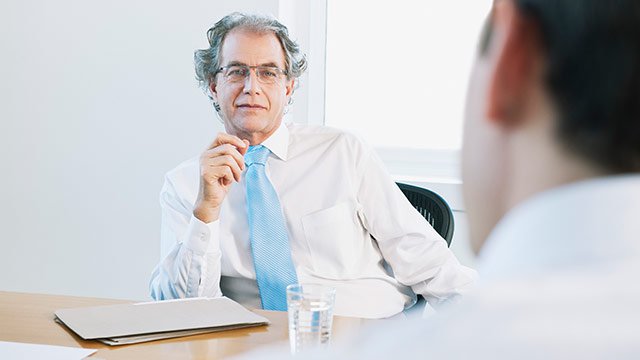 Two men talking across a table with glasses of water and paperwork on the table.