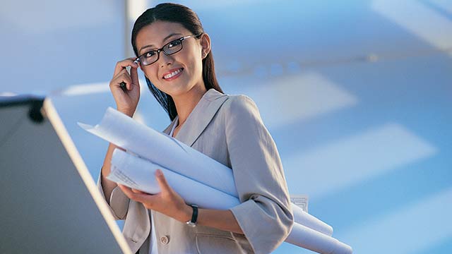 A man sitting in his office holding documents while smiling into the camera.