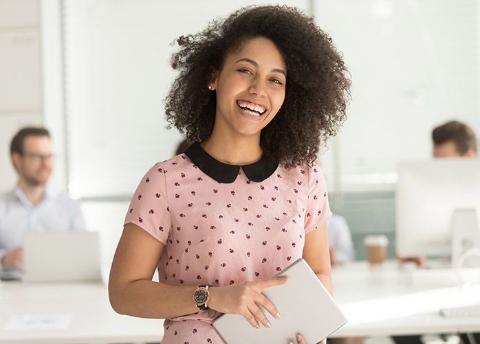 A woman wearing a pink shirt in an office holding a smart tablet.