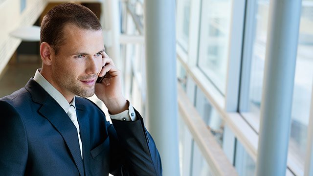 A man talking on the phone looking out of an office window.