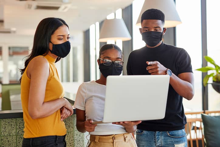Group of masked young businesspeople using a laptop in an office